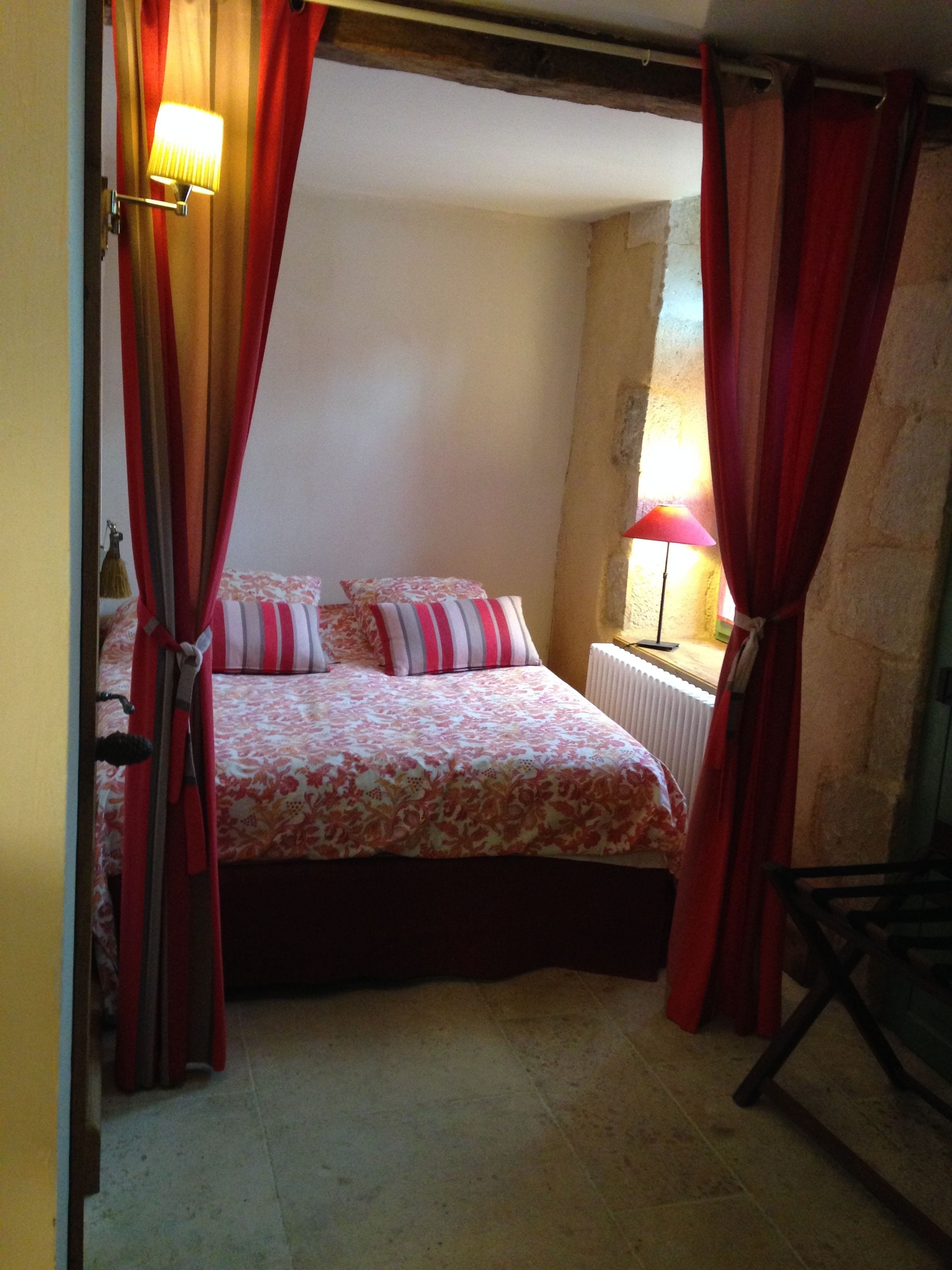 A bedroom with a bed, curtains, a lamp, and a radiator.