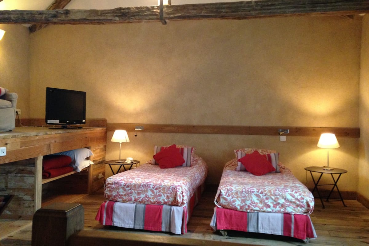 A cozy room with two beds, a television on a wooden shelf, and two bedside lamps.