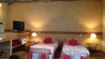 A cozy room with two beds, a television on a wooden shelf, and two bedside lamps.
