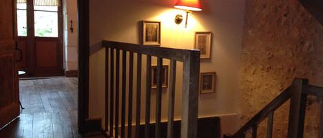 Una escalera de madera con barandilla, una lámpara de pared y cuadros enmarcados.