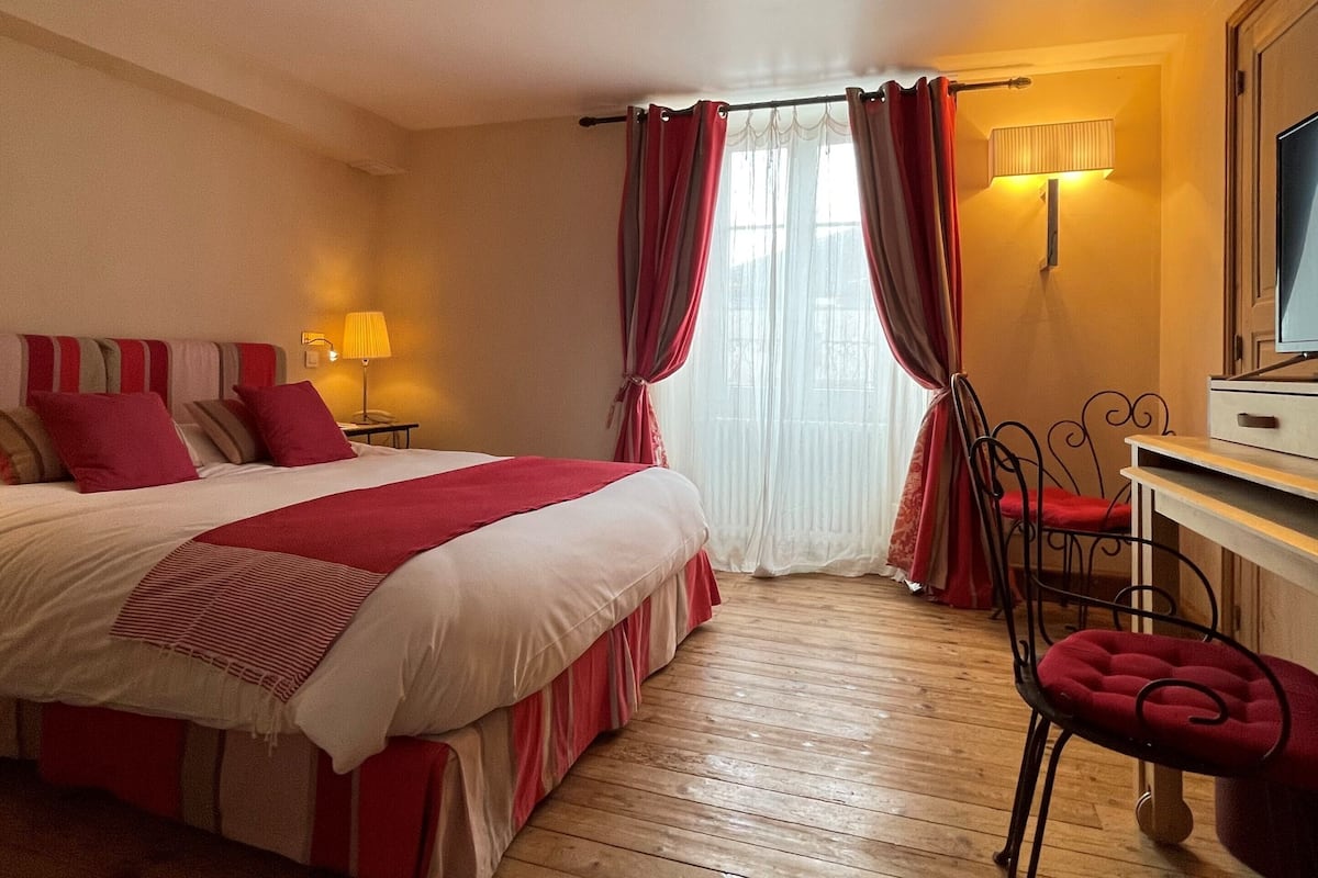 A hotel room with a bed, a desk, a chair, and a window with curtains.