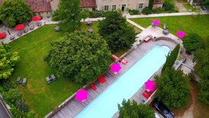 Piscina con muelle de madera, rodeada de césped y árboles. Hay sillones de descanso y sombrillas.