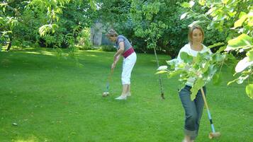 Two people playing croquet in a grassy area with trees in the background.