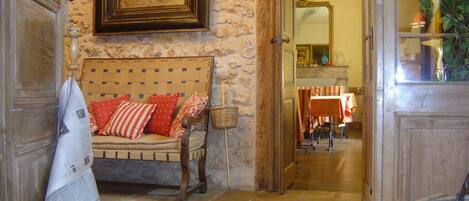 Una habitación acogedora con pared de piedra, un banco de madera con cojines rojos, una cesta de mimbre y un espejo sobre una mesa con mantel rojo y blanco.