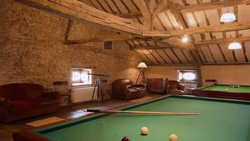 A billiards room with a pool table, leather chairs, and a stone wall.