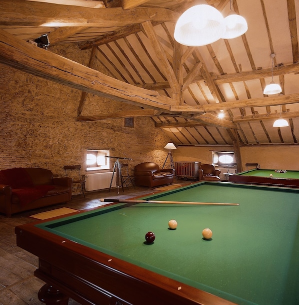 A billiards room with a pool table, leather chairs, and a stone wall.