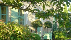 Un sendero en un jardín que lleva a un edificio de fachada de piedra y contraventanas verdes.