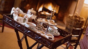 Una bandeja con té y pasteles sobre una mesa frente a una chimenea.