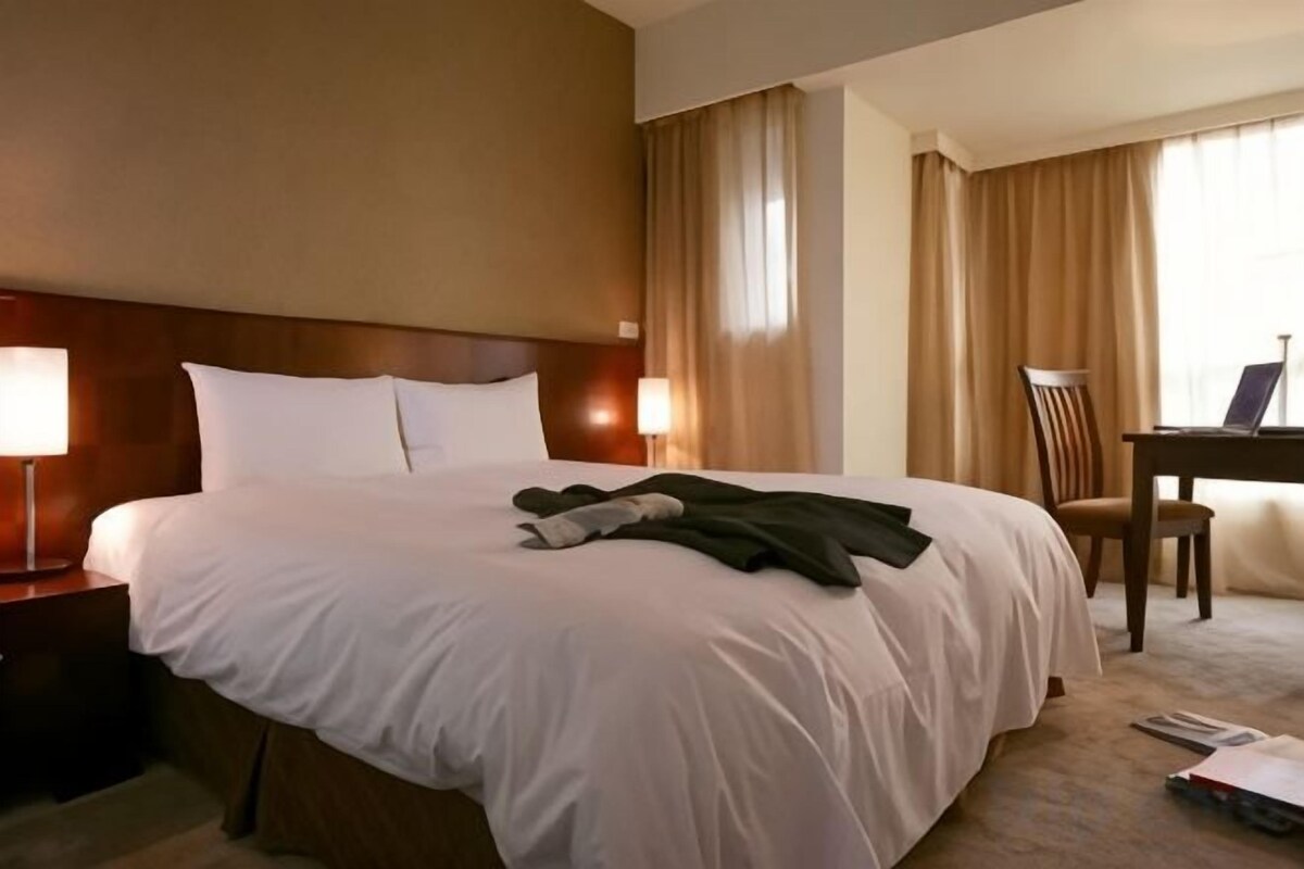 Hotellihuone, jossa on suuri sänky, työpöytä ja tuoli.