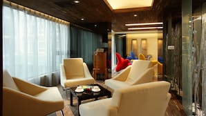 A modern hotel lobby with leather armchairs, a wooden cabinet, and a glass partition with decorative elements. - In One City Inn (Taichung)