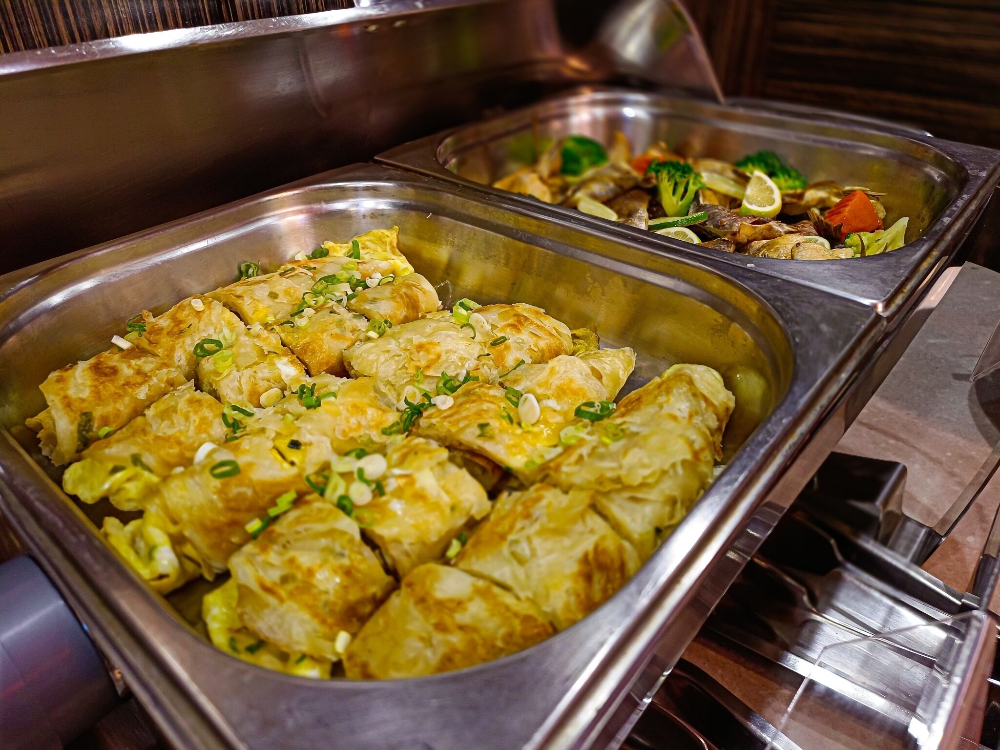 A buffet with various dishes including a tray of stuffed vegetables and another with mixed vegetables and meat.