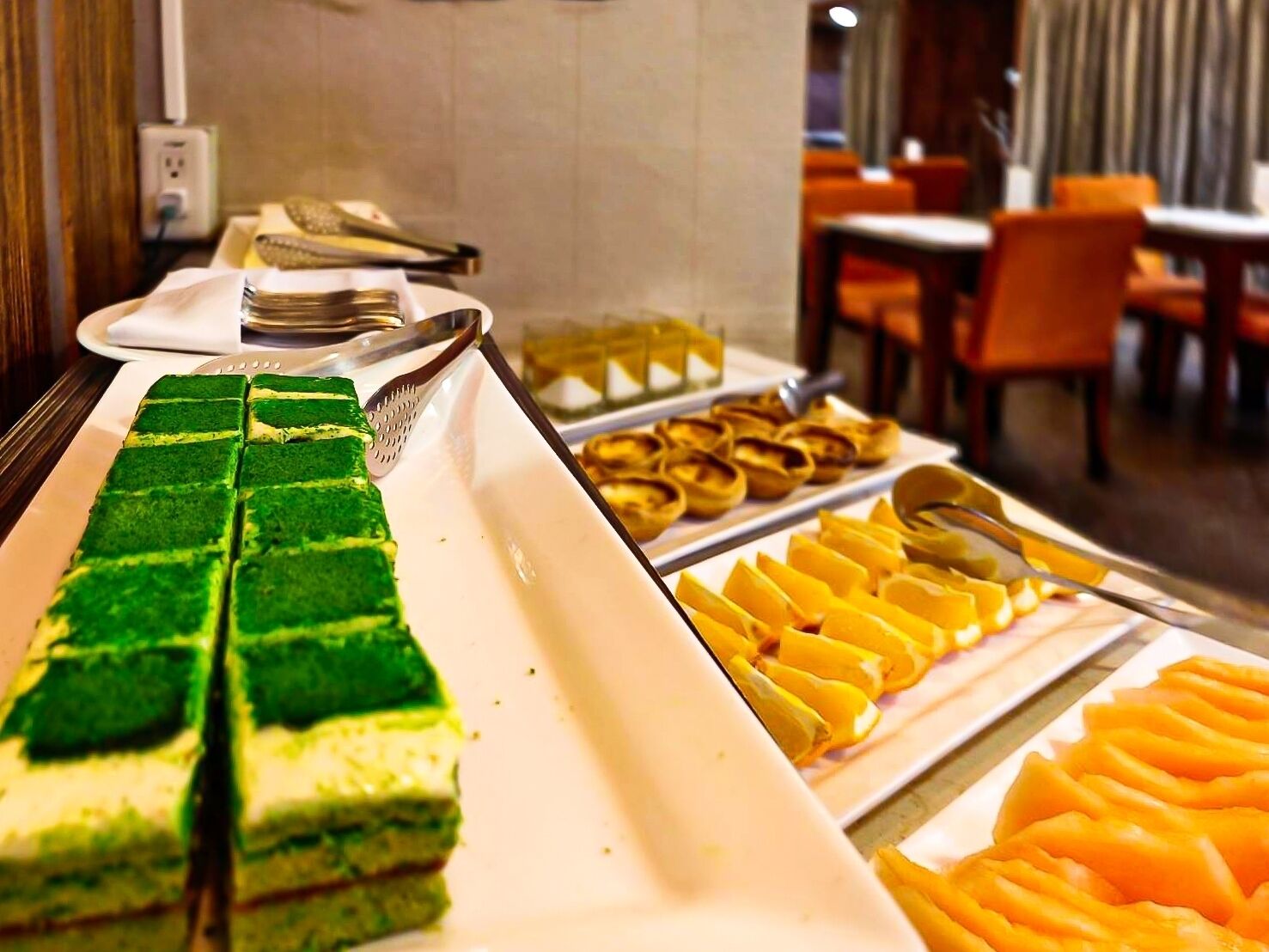 A buffet with various food items including green and yellow desserts and orange fruit slices.