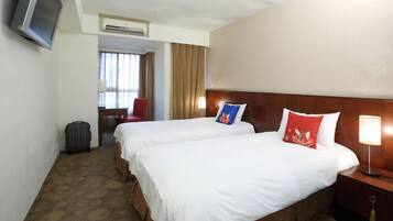 A hotel room with two beds, a television, a lamp, and a suitcase.