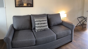 Un canapé gris avec un coussin à motifs, un lampadaire et un tableau encadré accroché au mur.