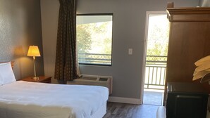 Habitación de hotel con cama, lámpara de noche, equipo de aire acondicionado y escritorio con microondas.
