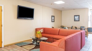 Un moderno vestíbulo de hotel con un sofá modular, un televisor de pantalla plana y un comedor con sillas y mesas.