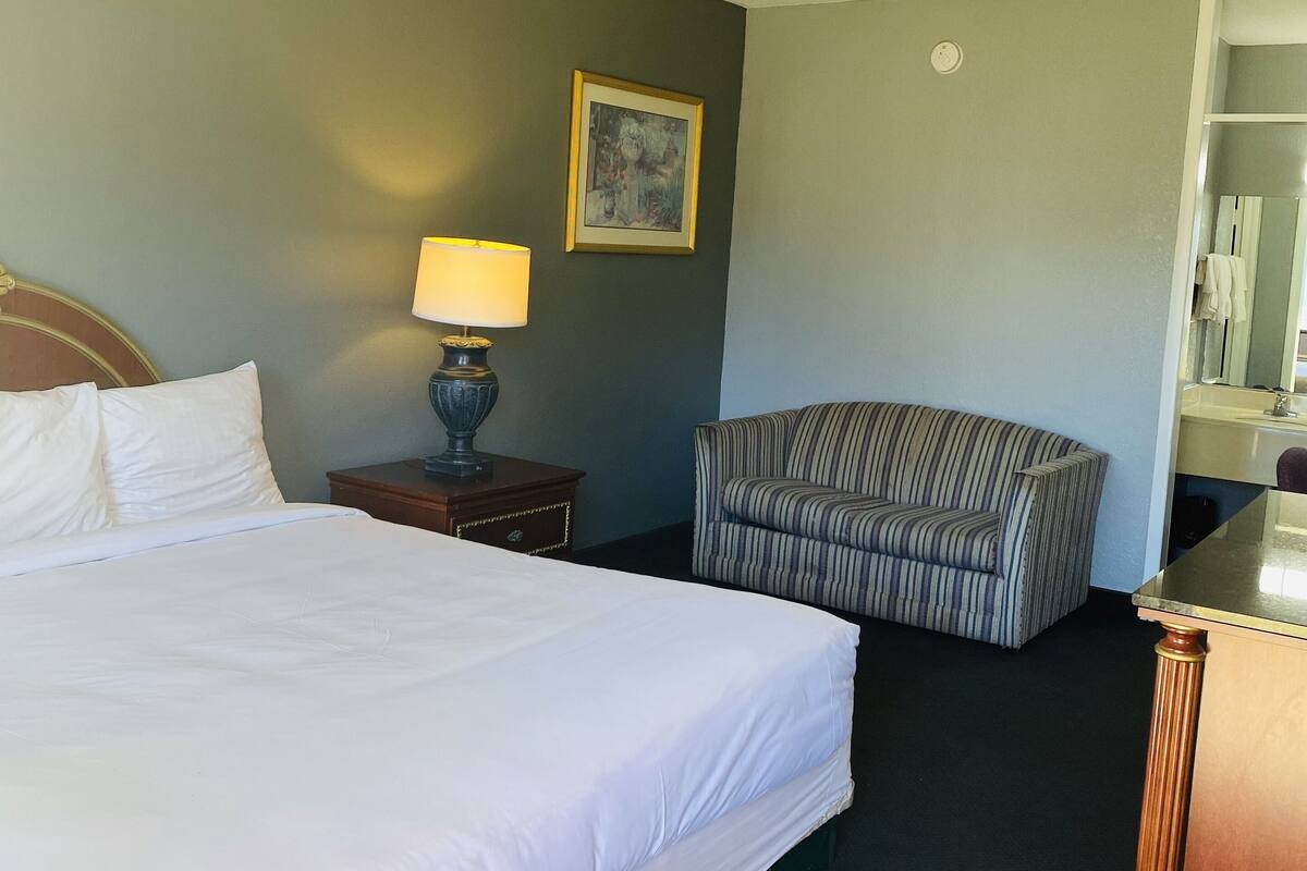 A hotel room with a large bed, a chair, a nightstand with a lamp, and a painting on the wall.