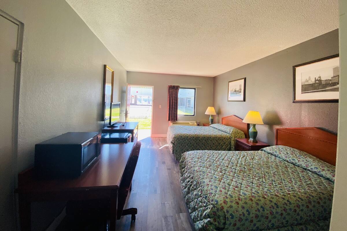 A hotel room with two beds, a desk with a computer, a TV, and a window with curtains.