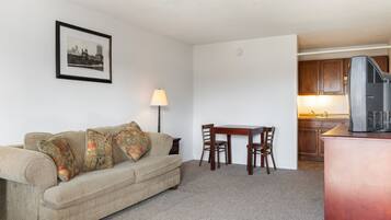 A living room with a sofa, a table, and chairs, a lamp, and a kitchen area with cabinets and a microwave.