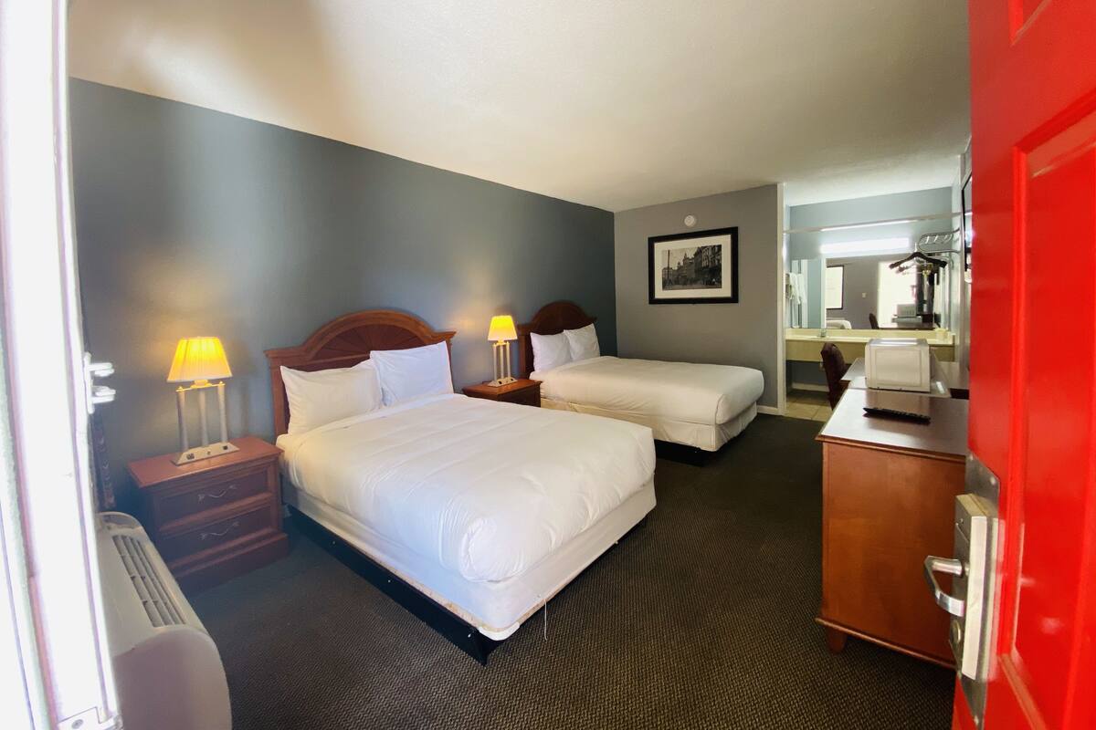 A hotel room with two beds, a desk, a chair, a dresser, a mirror, and a picture on the wall.