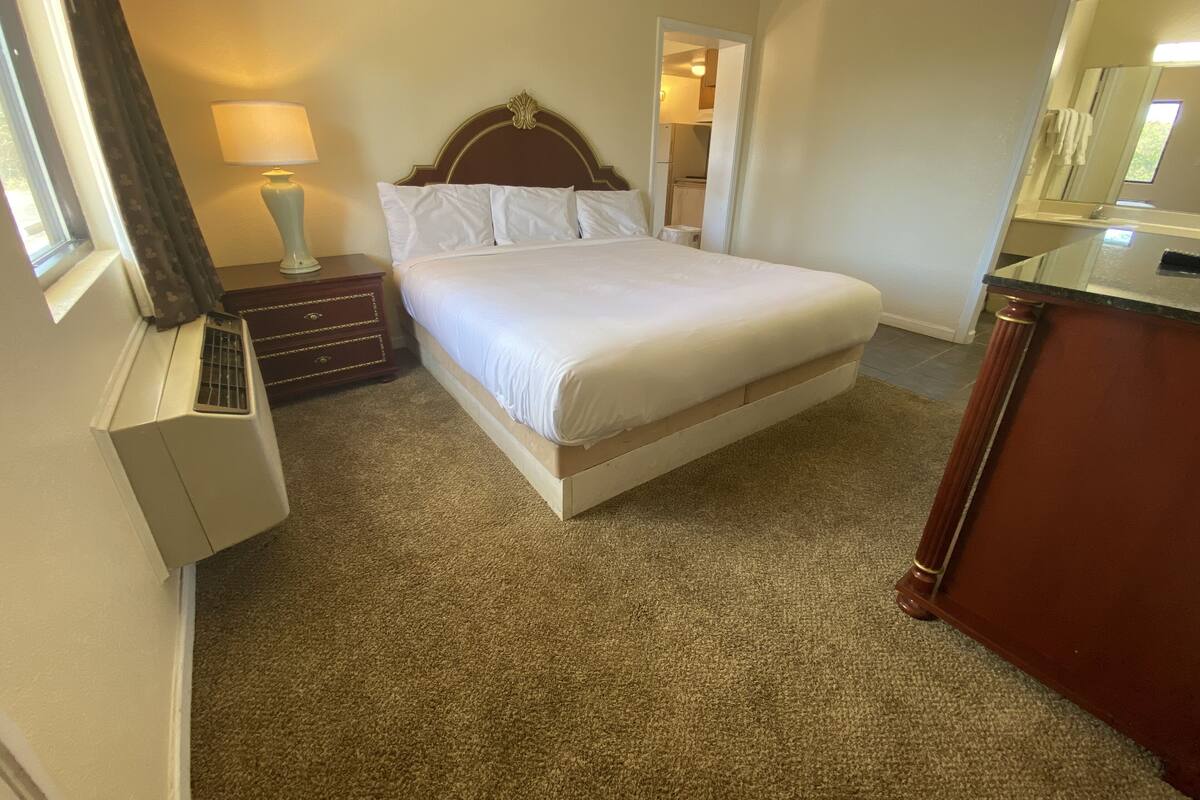 A hotel room with a bed, a dresser, a lamp, and a window with curtains.