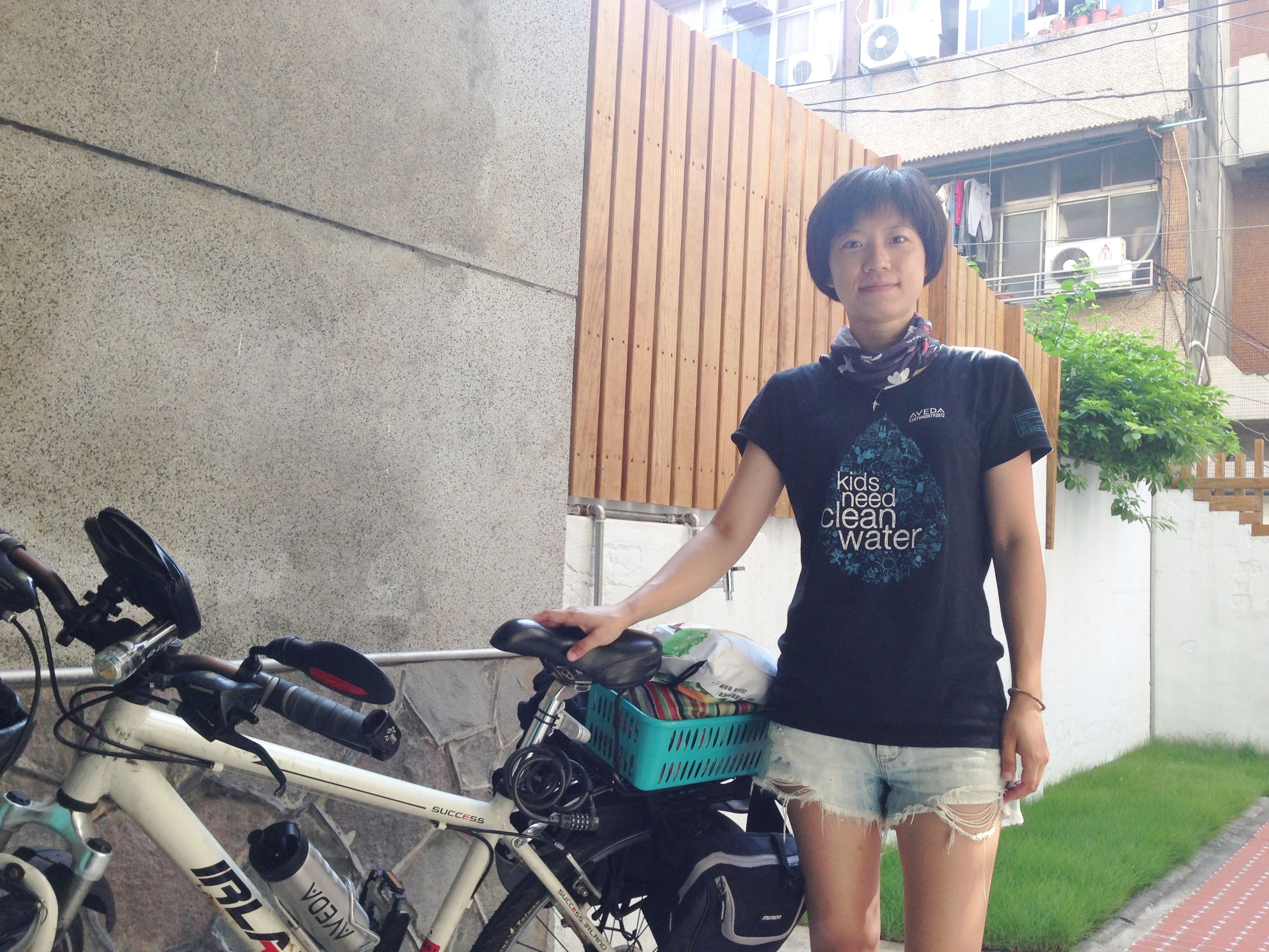 A person standing next to a bicycle with a basket containing various items.