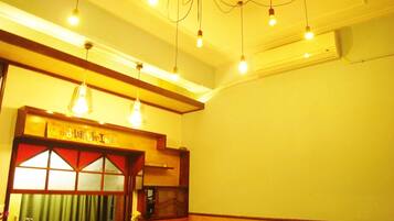 A hotel room with a reception desk, a red bench, a patterned bench, a trash bin, and a ceiling with hanging lights.