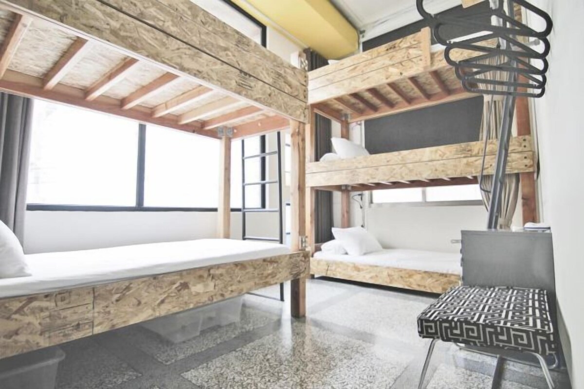 Habitación con literas, techo de madera, una pequeña mesa y una ventana.