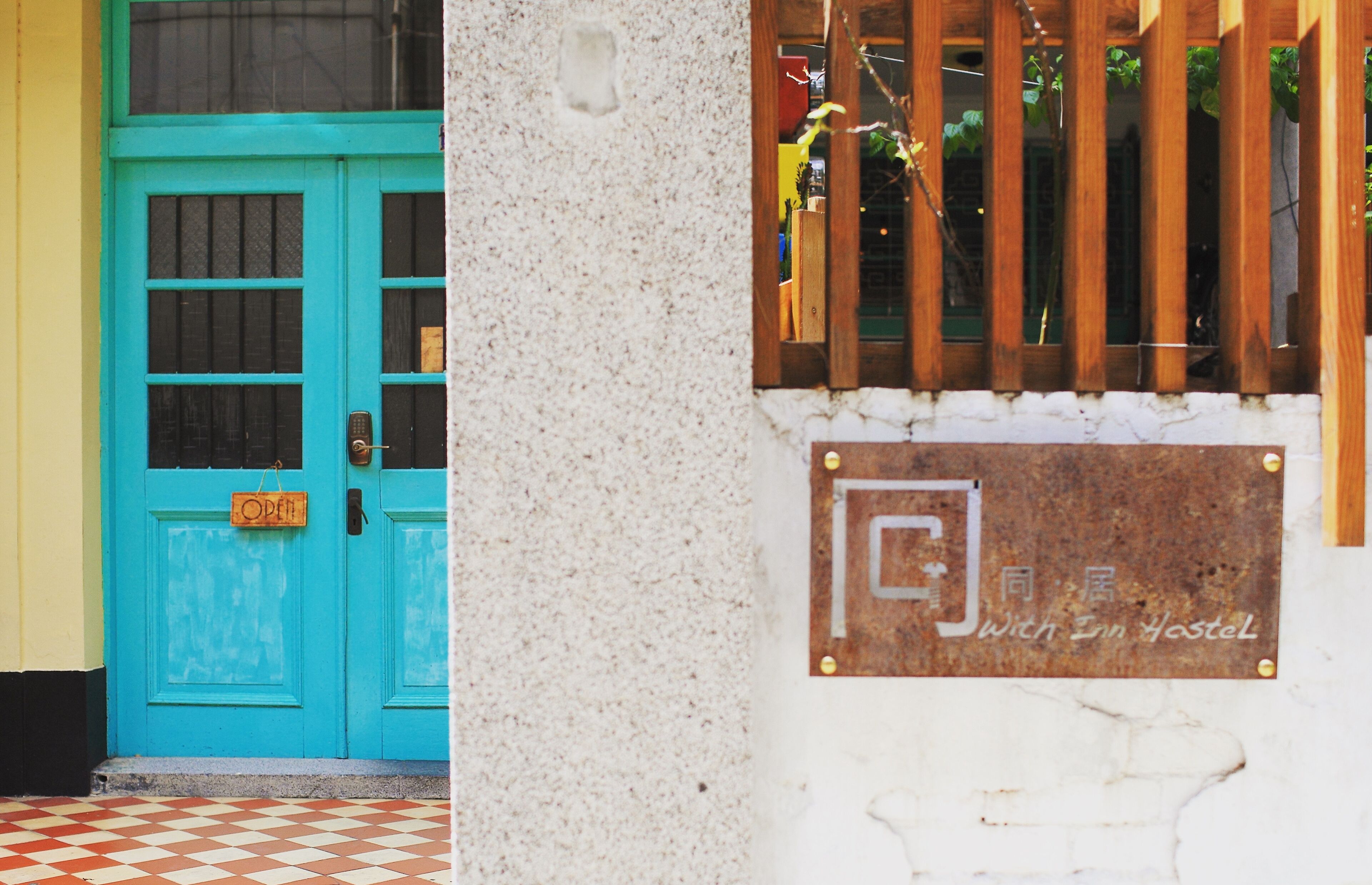 Une porte turquoise avec une enseigne indiquant « OUVERT » et une plaque portant des caractères chinois ainsi que le texte « With Inn Hostel ».