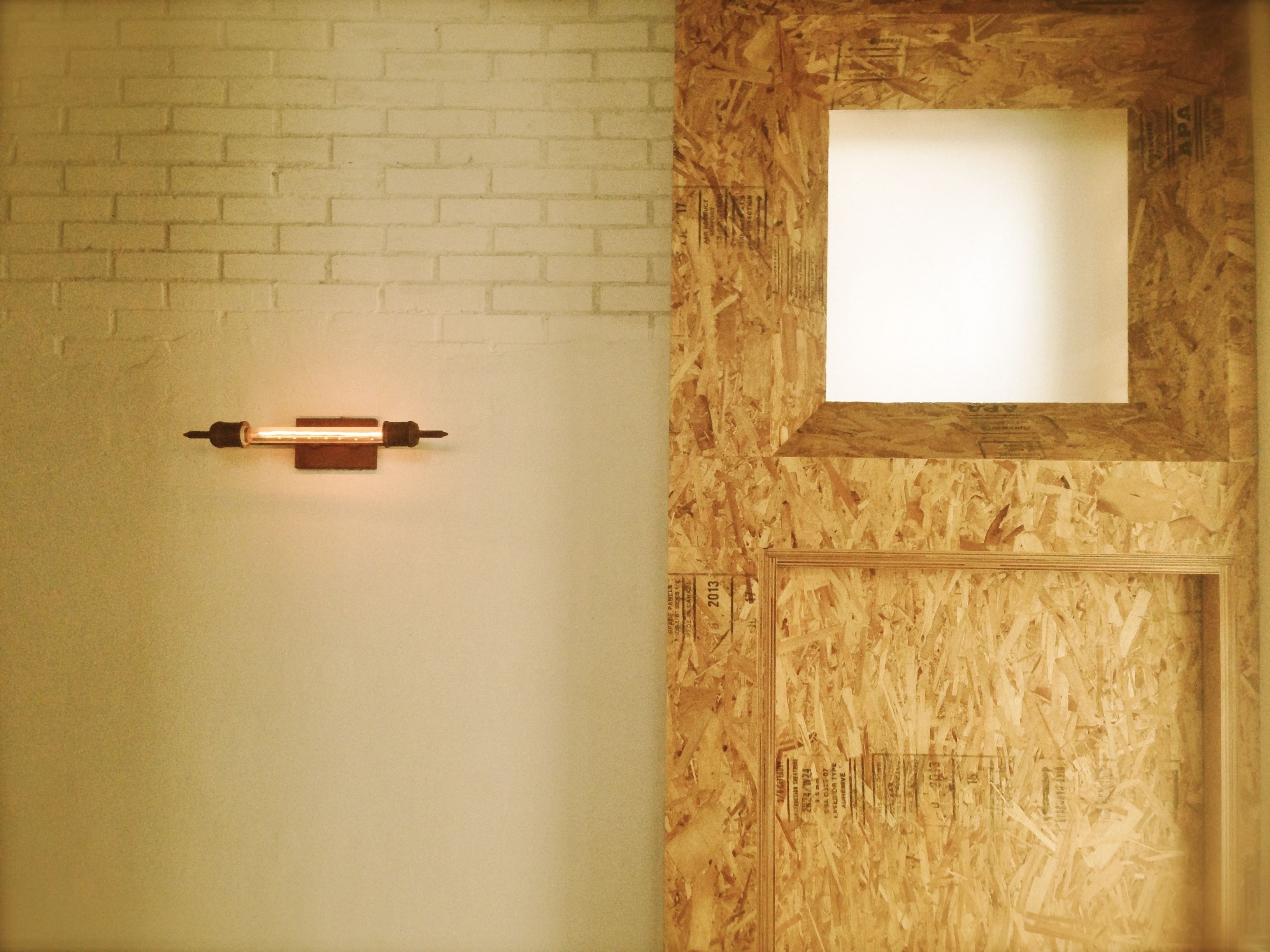 A room with a white brick wall, a wooden door with a window, and a wall-mounted light fixture.