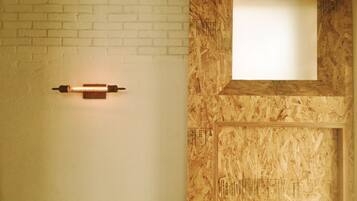 A room with a white brick wall, a wooden door with a window, and a wall-mounted light fixture.