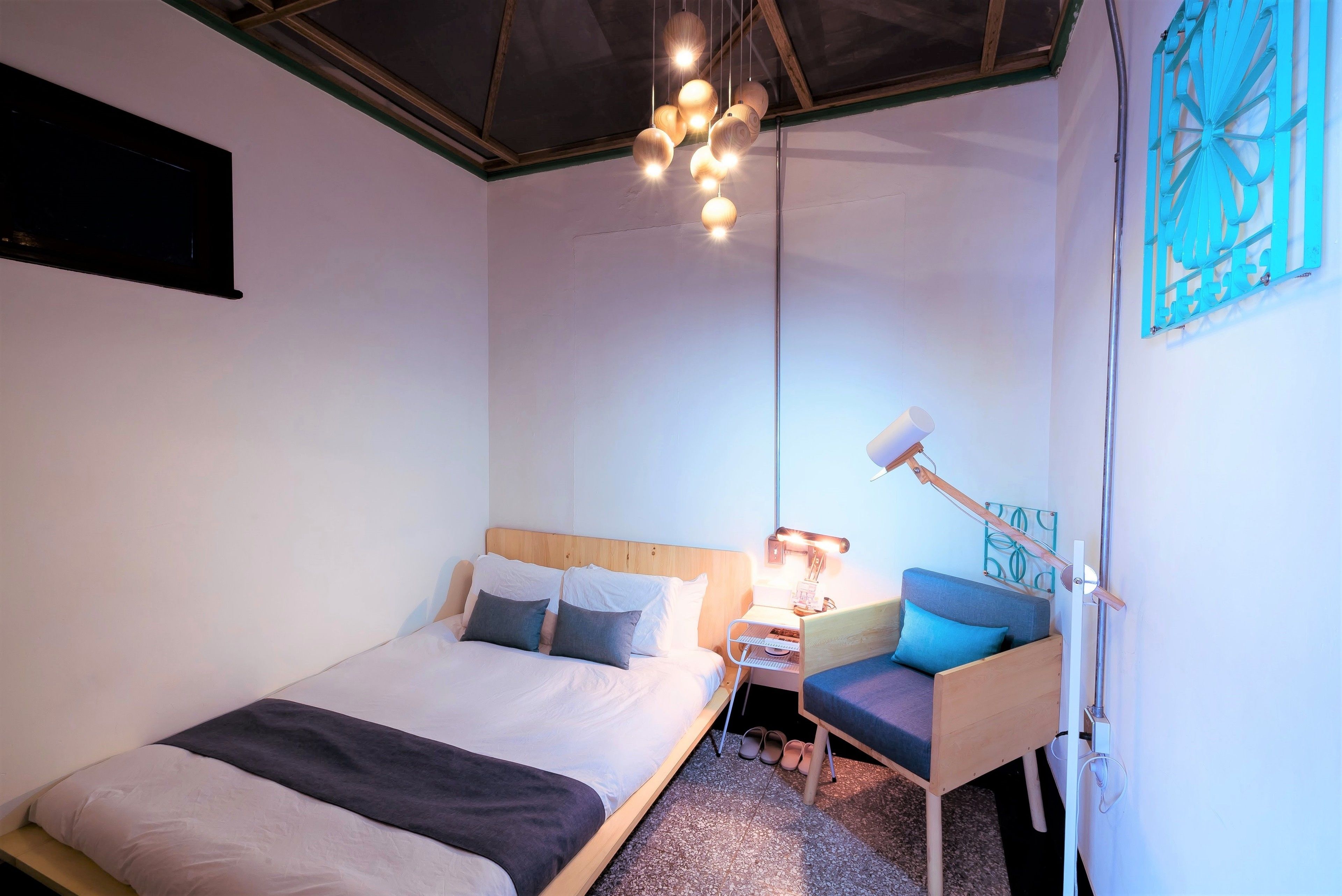 A modern hotel room with a large bed, bedside table, and a small seating area.