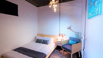 A modern hotel room with a large bed, bedside table, and a small seating area.