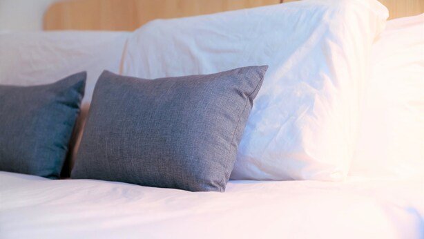 Een bed met witte lakens en twee grijze kussens.