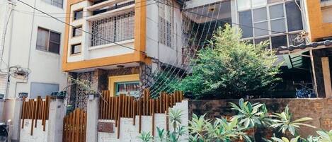 Un immeuble résidentiel au design moderne, doté d’une entrée sécurisée par un portail, d’un balcon avec une rambarde en métal et de plantes en pot disposées au premier plan.