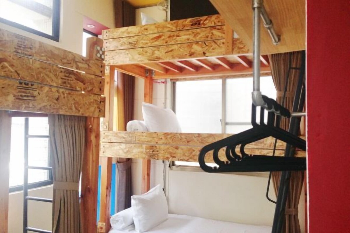 A compact room with a bunk bed, a window with curtains, and a wooden ceiling.