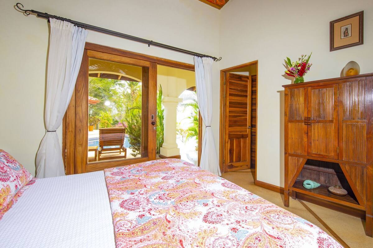 A bedroom with a bed, a wooden wardrobe, a chair, and a view of an outdoor area.