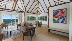 Amplia sala de estar con techos altos, vigas de madera, un ventanal con vistas al exterior, un comedor y una obra de arte colorida en la pared.