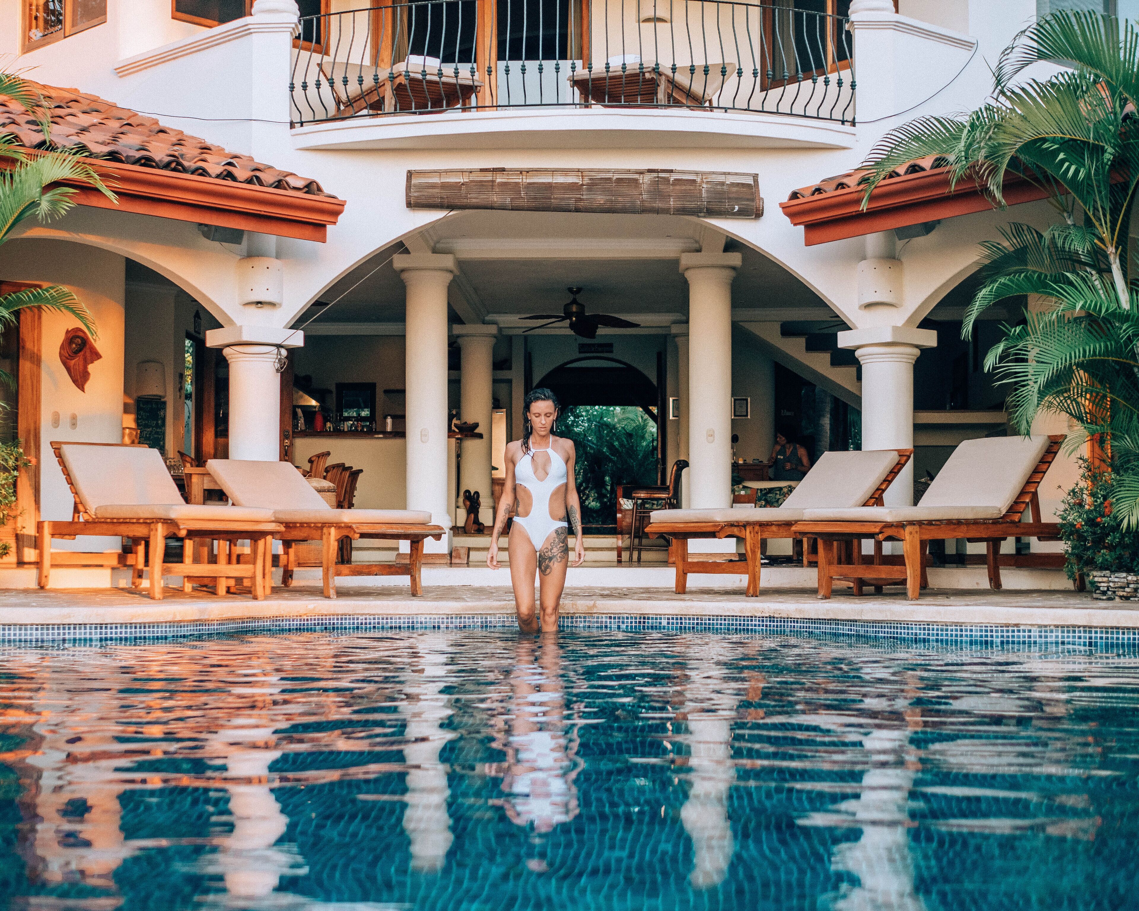 A pool area with lounge chairs and a person in a swimsuit.