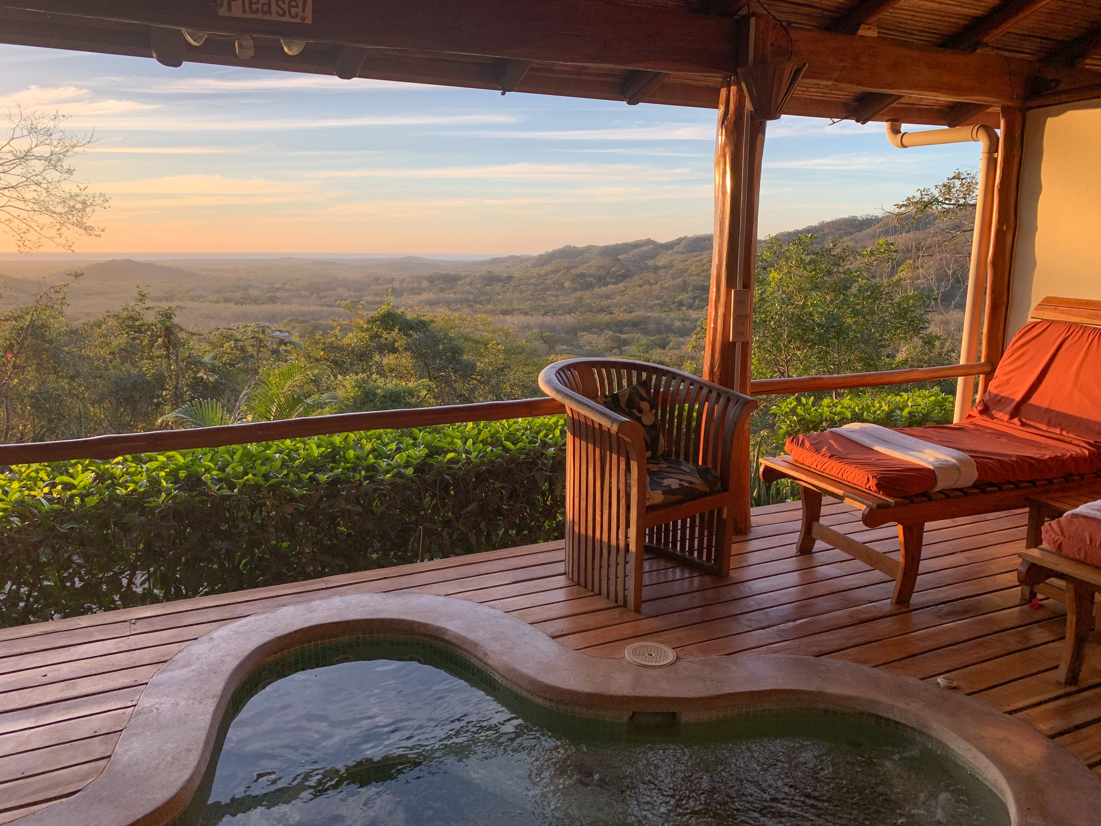 Una terraza de madera con un jacuzzi, una silla de madera y una cama con una manta roja.