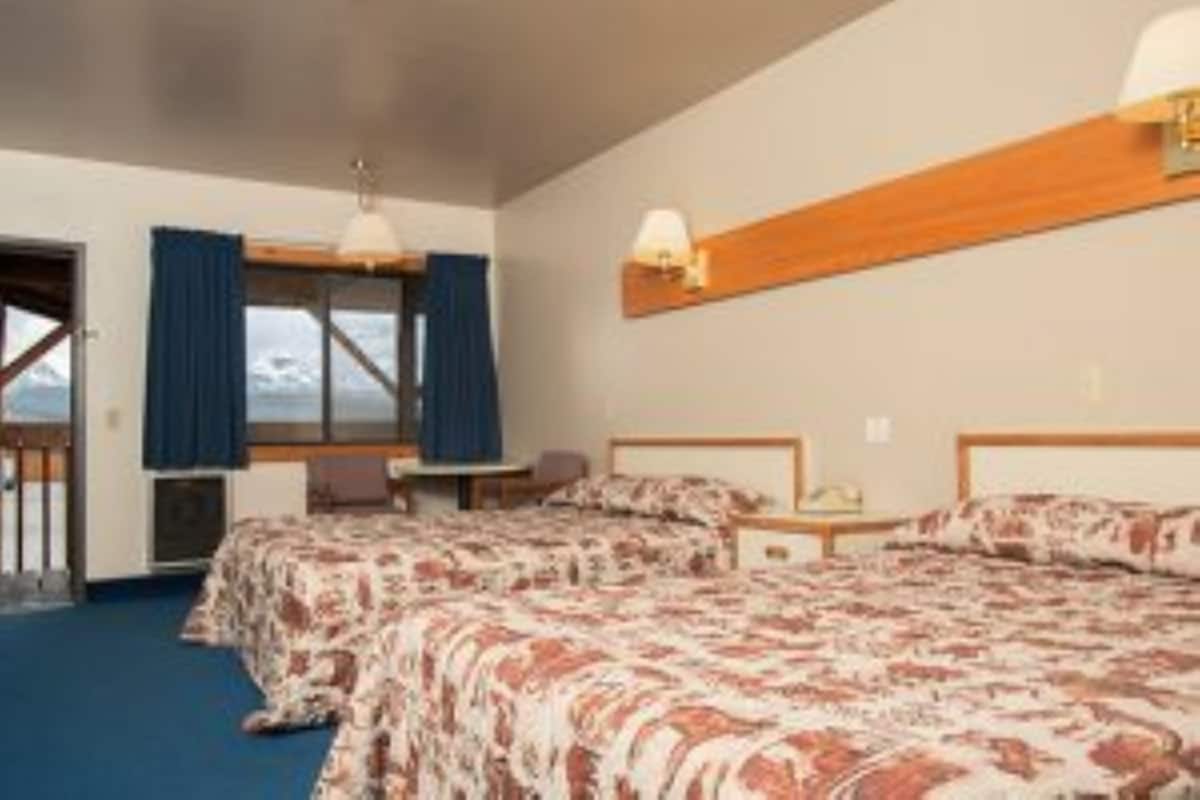 A hotel room with two beds, a desk, and a window with curtains.