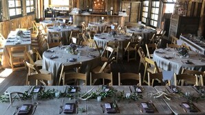 A rustic dining area with round tables set for multiple guests, wooden chairs, and a bar area in the background. - Mountain Village Lodge (Stanley)