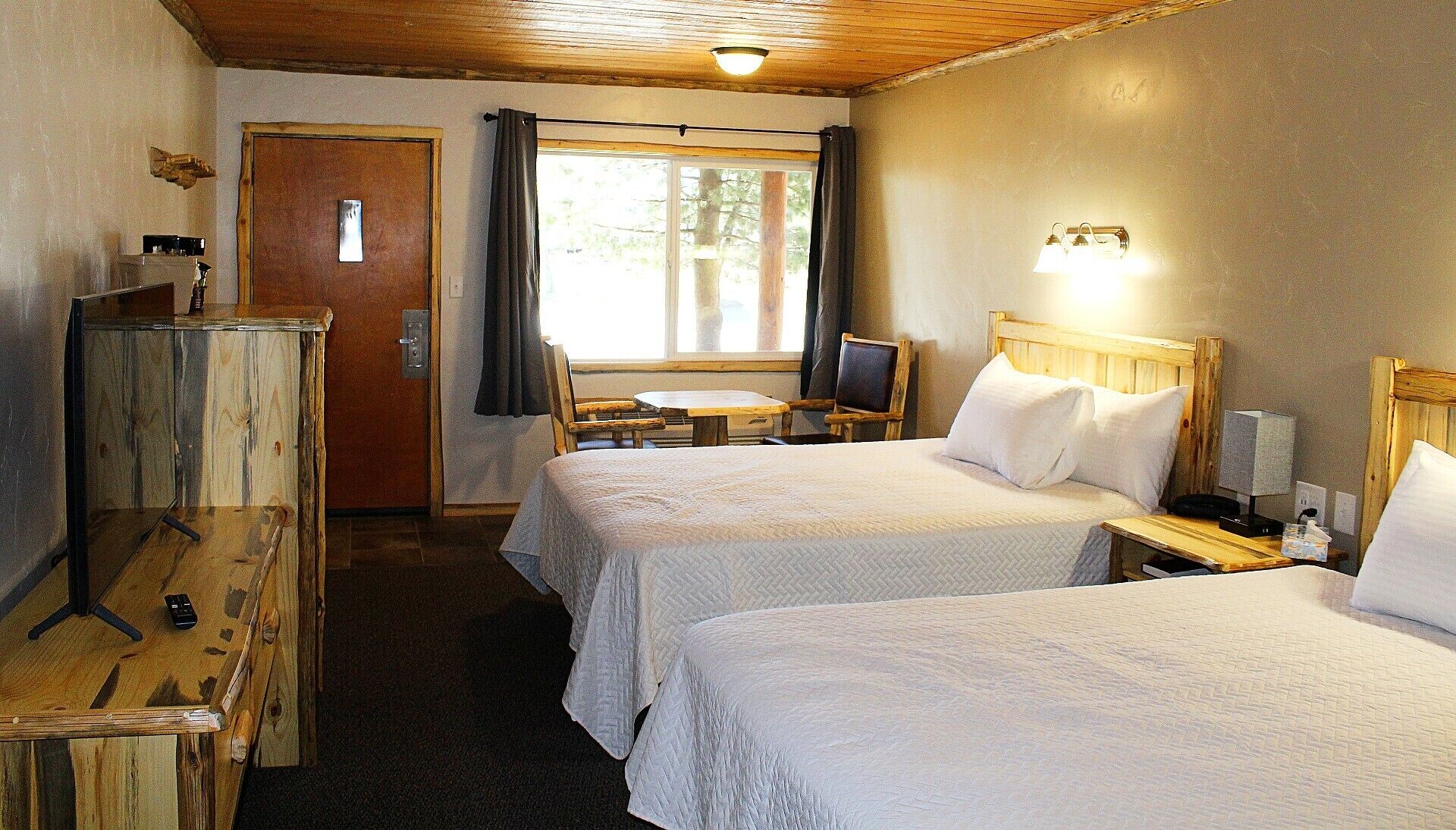 A hotel room with two beds, a desk, a chair, a TV, and a wooden dresser.