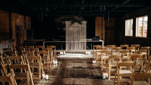 A rustic venue with wooden chairs arranged in rows facing a stage with a decorative backdrop. - Mountain Village Lodge (Stanley)