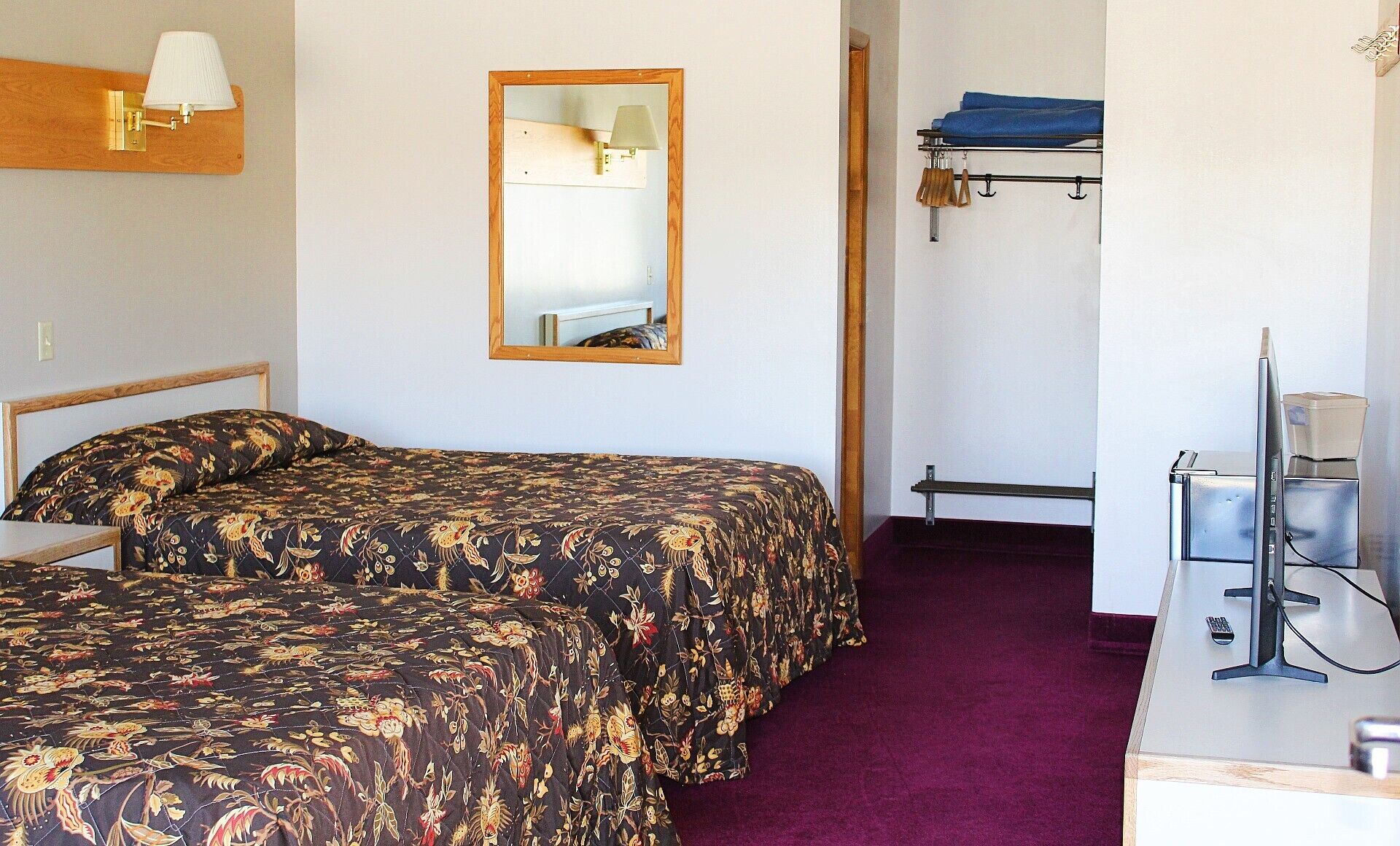 A room with two beds, a mirror, a lamp, a TV, and a coat rack.