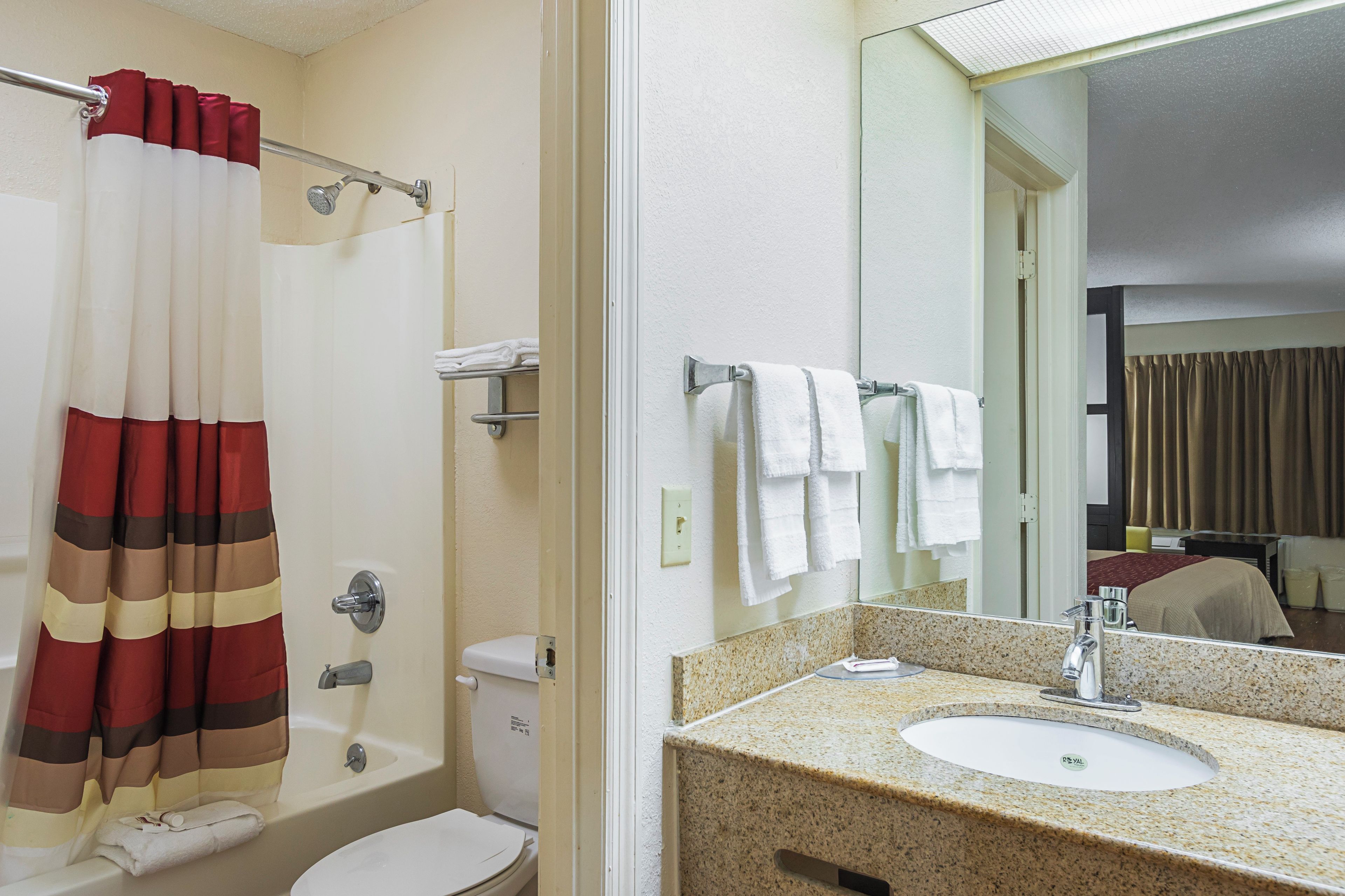 Ein Hotelbad mit Duschvorhang, Toilette, Waschbecken mit Spiegel und Handtuchhalter.