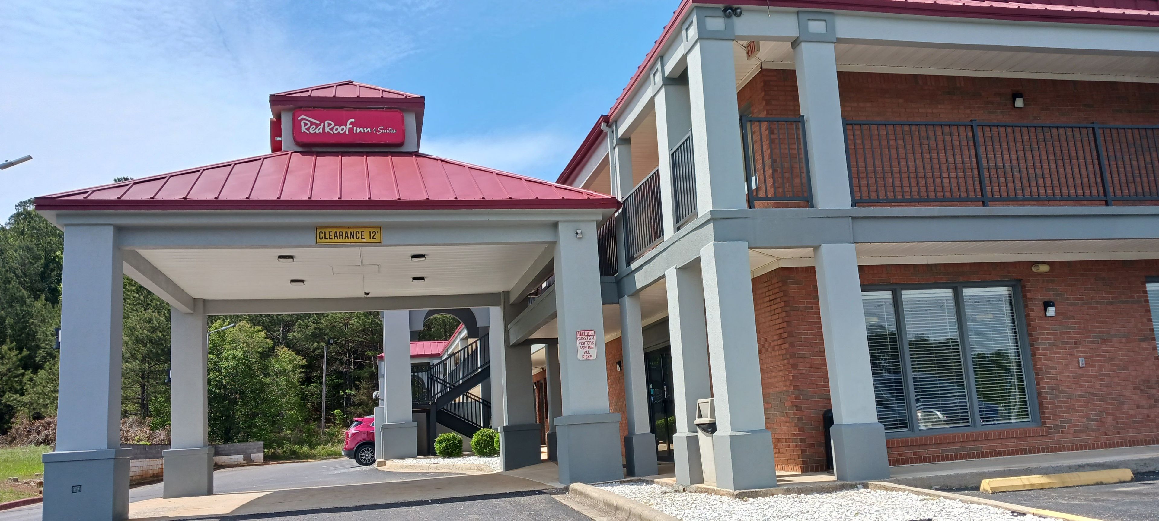A Red Roof Inn & Suites with a covered entrance, a clear sign indicating a 12-foot clearance, and a staircase leading to the upper level.