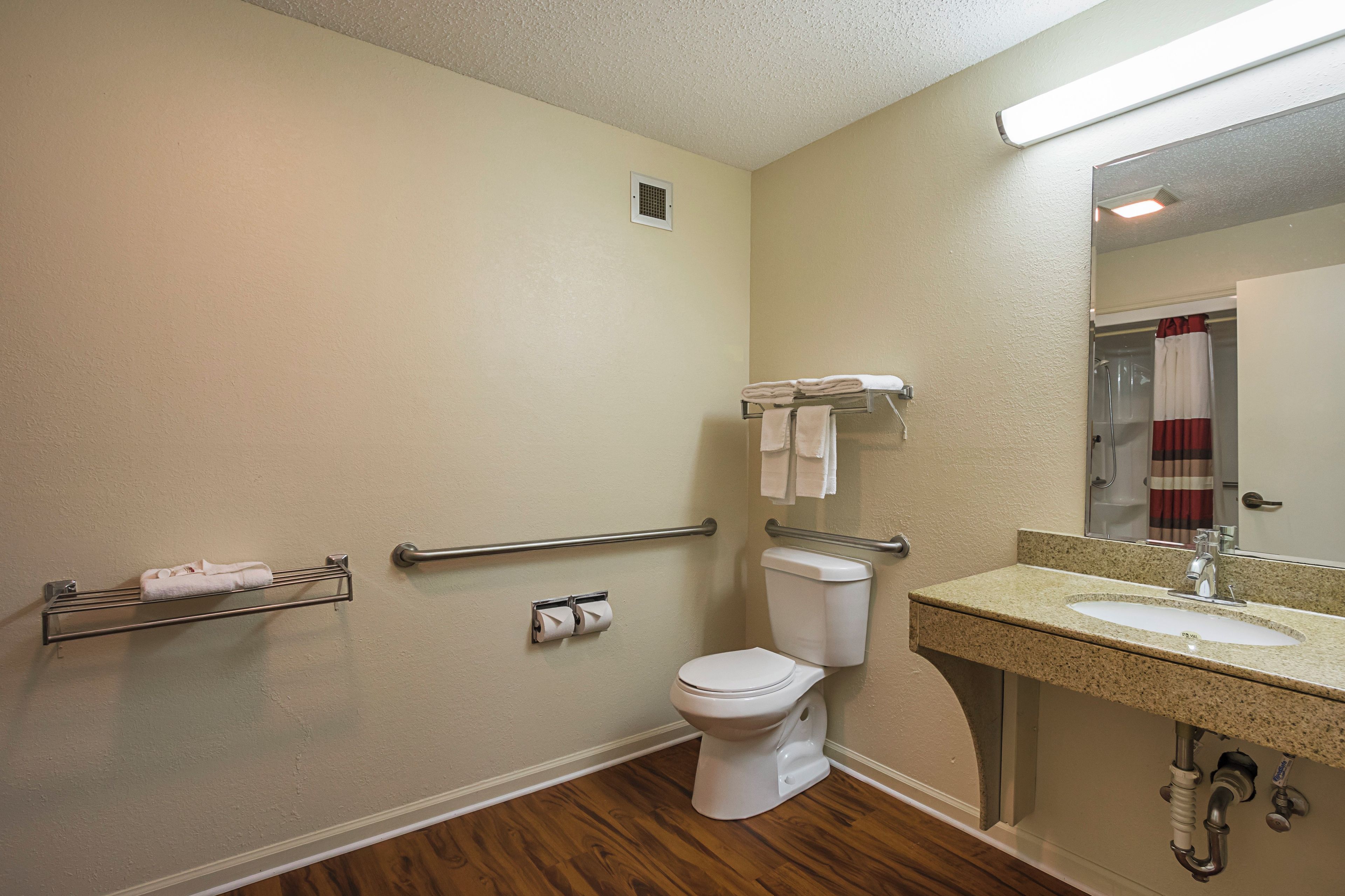 A bathroom with a toilet, sink, towel rack, and handrails.