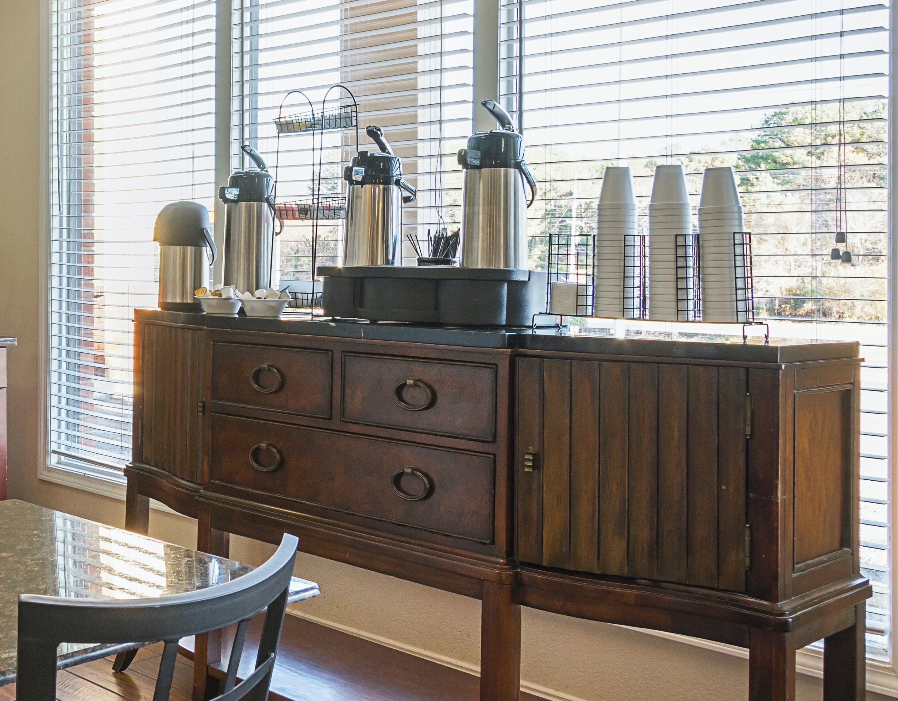 A wooden cabinet with drawers and a glass-top table, positioned near a window with blinds.