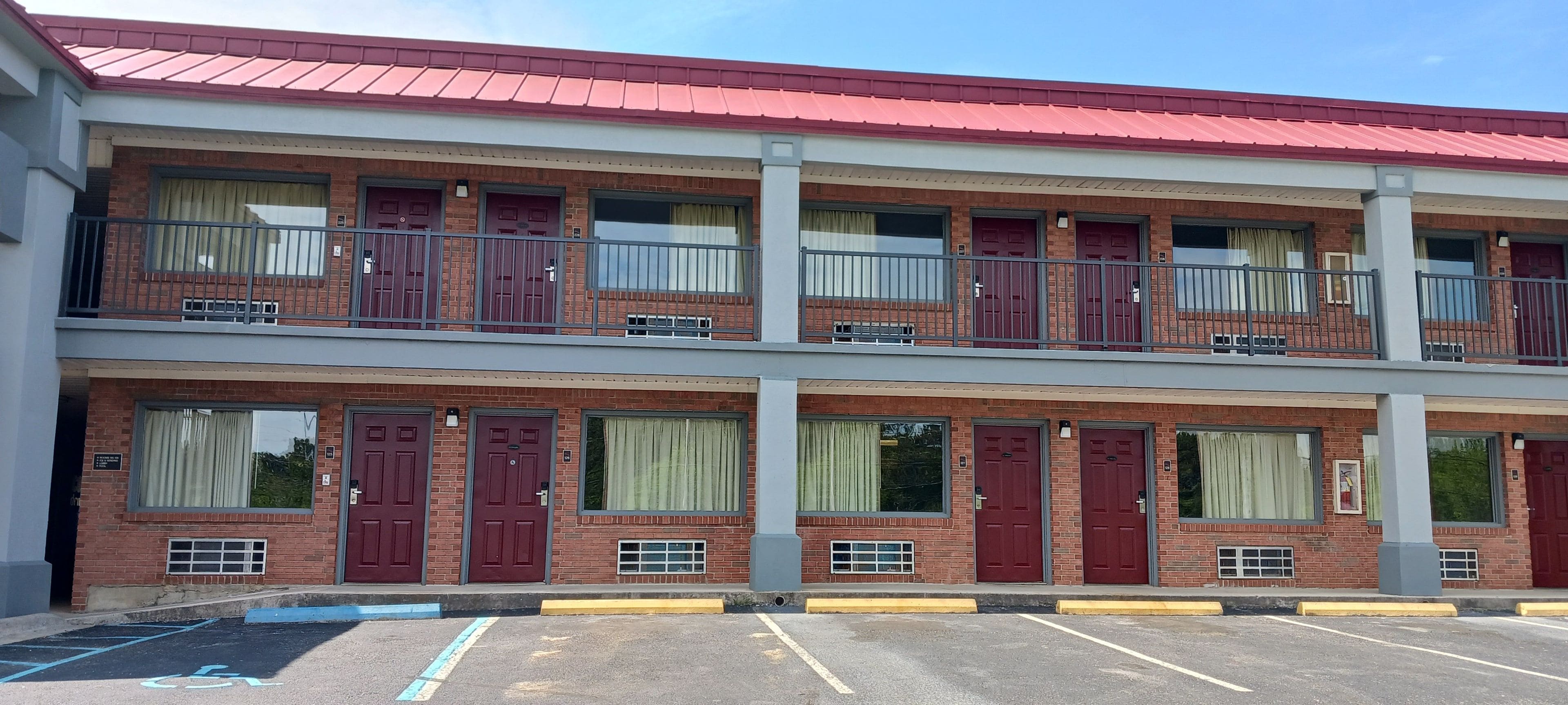 A two-story motel with red doors and windows, a red roof, and a parking lot with marked handicapped spaces.